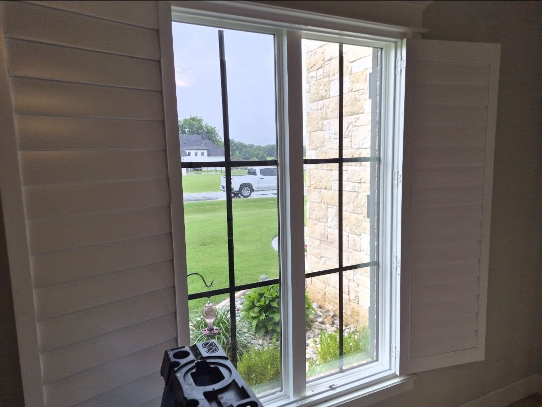 Tinted residential window with shutters overlooking backyard